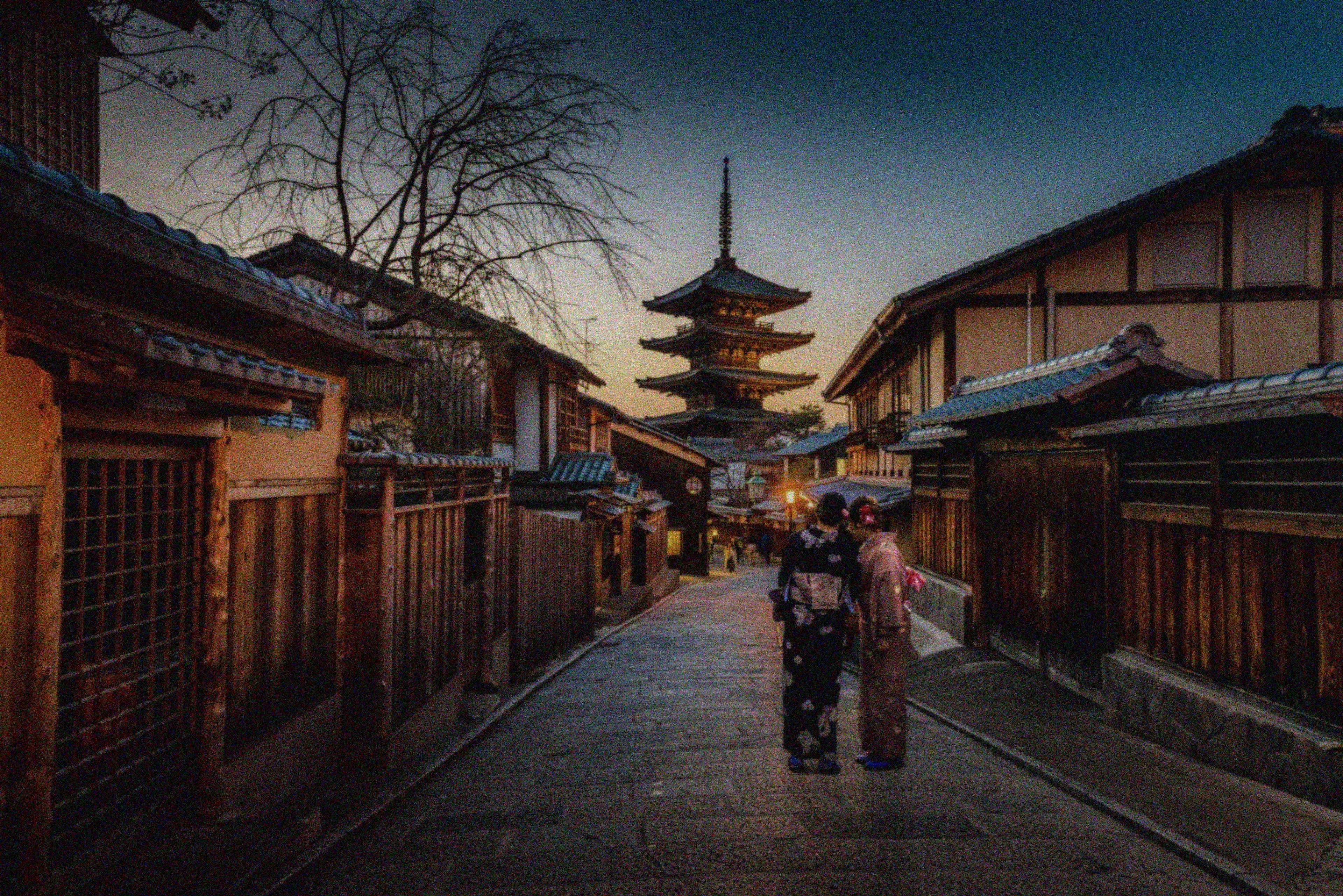 The same Kyoto street at dusk, grainy and dim as a small phone sensor would record it.
